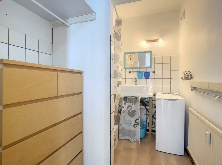Salle de bain minimaliste avec lavabo, machine à laver, rangement en bois et espace organisé.