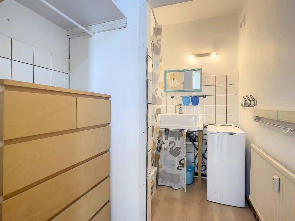 Salle de bain minimaliste avec lavabo, machine à laver, rangement en bois et espace organisé.