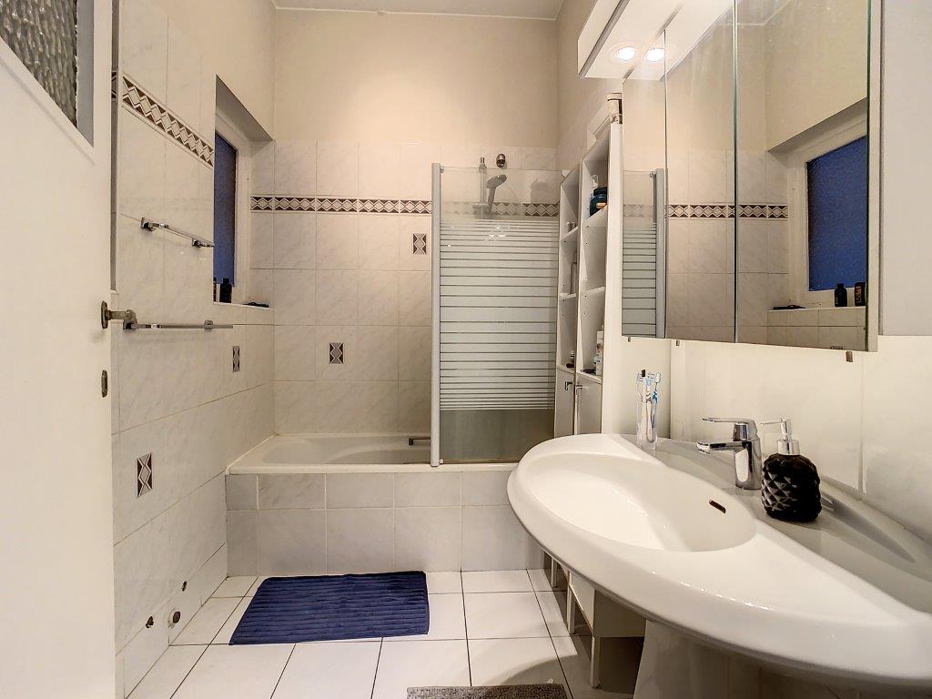 Salle de bain contemporaine épurée avec baignoire, douche en verre, grand lavabo et éclairage moderne.