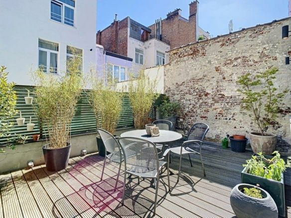Sunny urban terrace with modern furniture, green plants and brick wall.