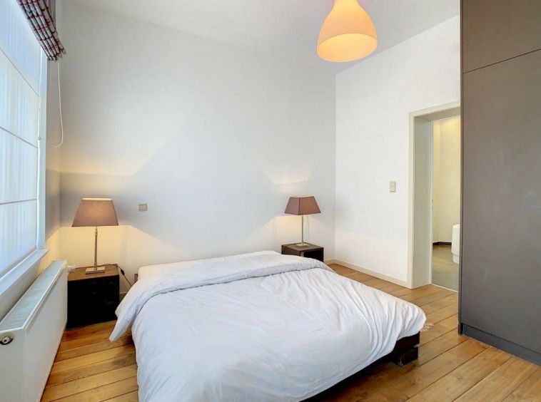 Chambre minimaliste lumineuse avec lit blanc, bois clair, lumière naturelle, ambiance sereine et chaleureuse.