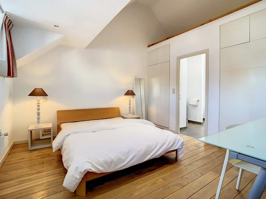 Chambre contemporaine lumineuse avec lit en bois, miroir, bureau en verre et ambiance apaisante.