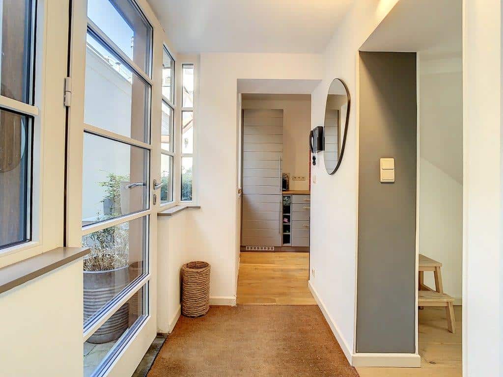 Hall moderne lumineux avec murs blancs, miroir rond et décor minimaliste.