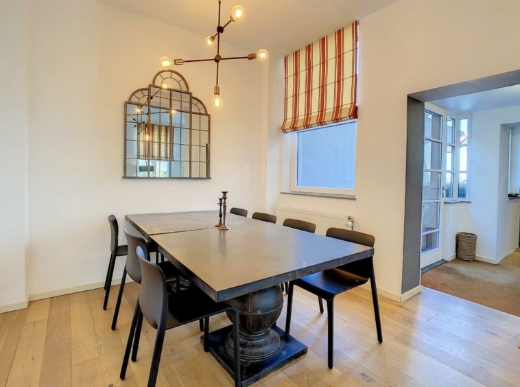 Salle à manger moderne avec table industrielle, éclairage design, lumière naturelle et miroir élégant.