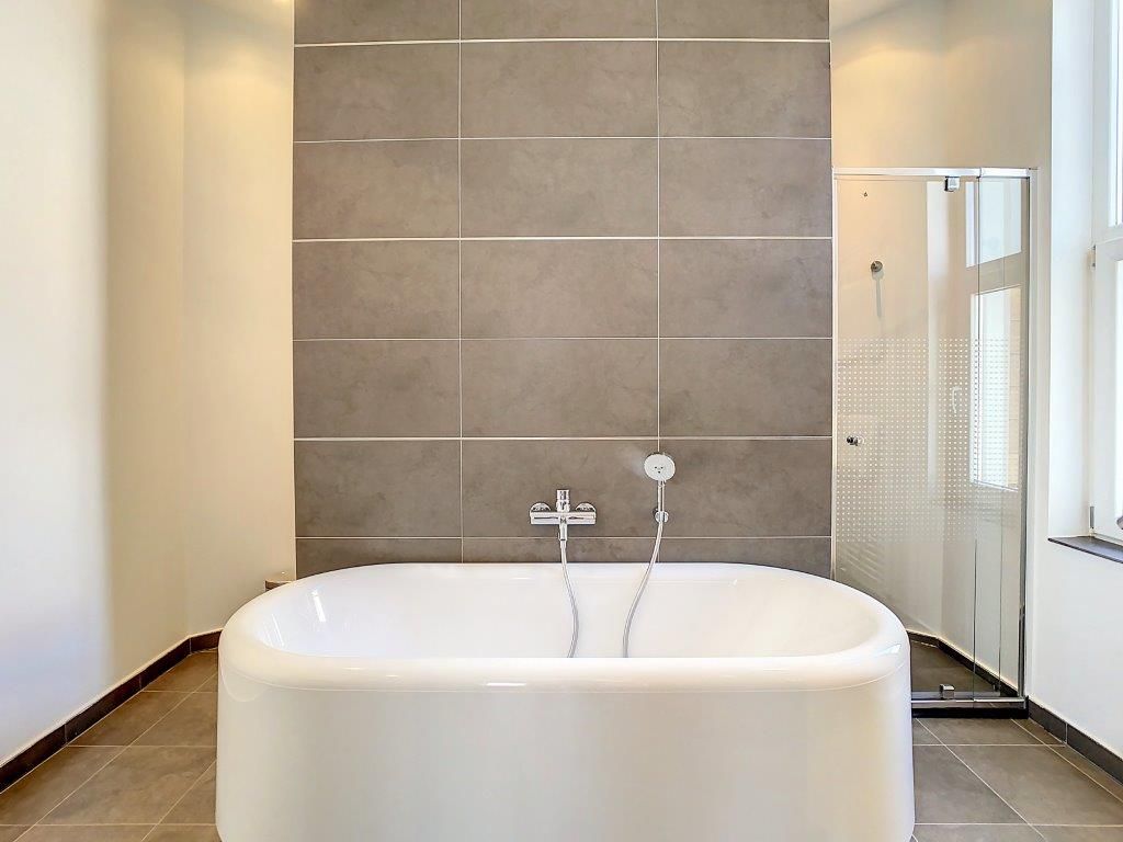 Salle de bain moderne avec baignoire blanche, douche en verre et ambiance lumineuse élégante.