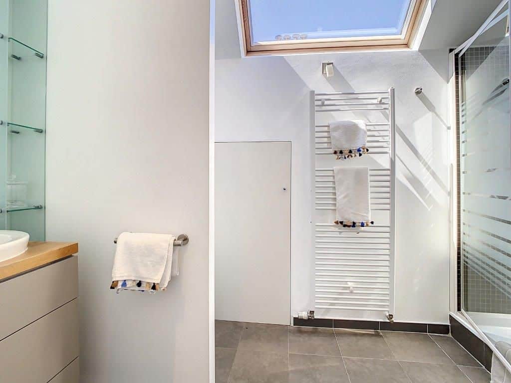 Salle de bain moderne avec douche en verre, lumière naturelle, rangements épurés et radiateur design.