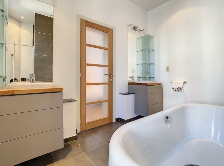 Salle de bain moderne avec baignoire design, double lavabo en bois, ambiance lumineuse et épurée.