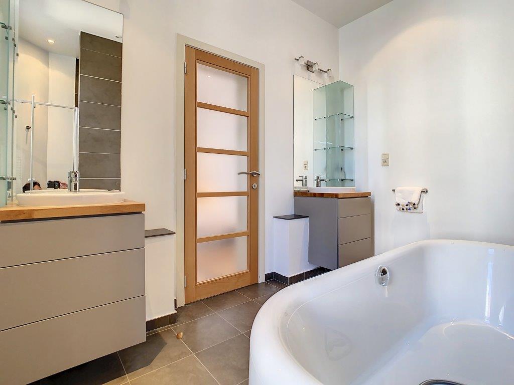 Salle de bain moderne avec baignoire design, double lavabo en bois, ambiance lumineuse et épurée.