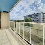 Balcon lumineux avec vue urbaine, arbres, ciel bleu et nuages blancs, idéal pour la détente.