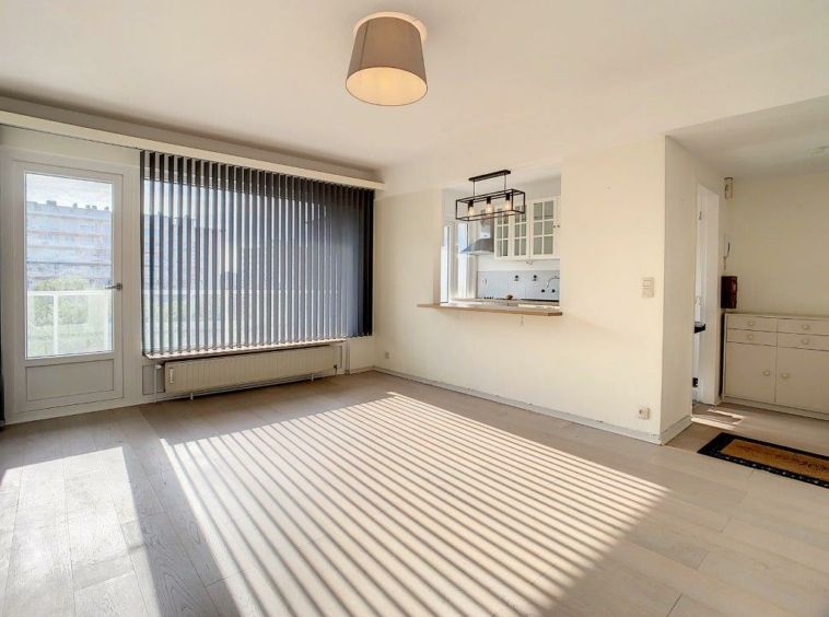 Salon moderne lumineux avec cuisine ouverte, grande fenêtre, lumière naturelle, décor minimaliste.
