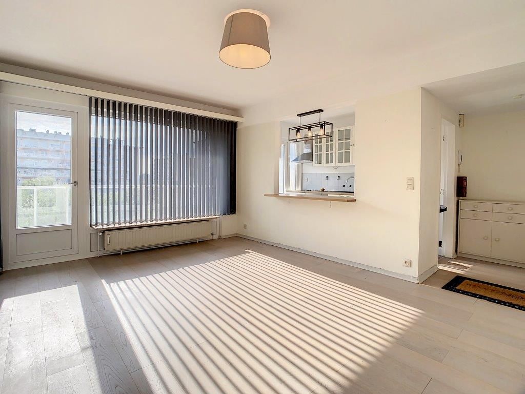 Salon moderne lumineux avec cuisine ouverte, grande fenêtre, lumière naturelle, décor minimaliste.