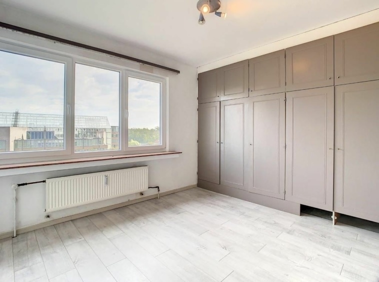 Espace lumineux et minimaliste avec grande fenêtre, rangement intégré et décoration adaptable.