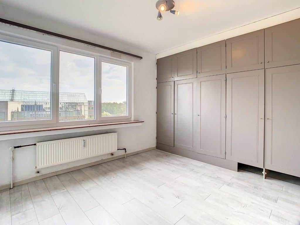 Espace lumineux et minimaliste avec grande fenêtre, rangement intégré et décoration adaptable.
