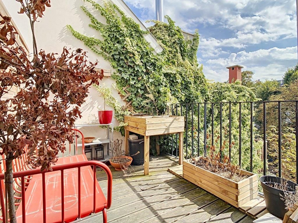 Balcon cosy avec banc rouge, plantes grimpantes, jardinière en bois et ciel paisible.
