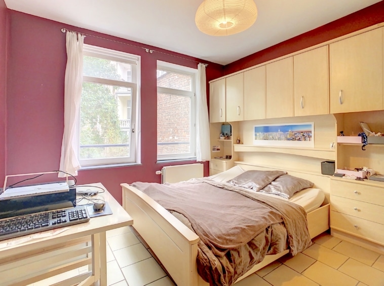 Chambre moderne et cosy avec mur bordeaux, luminosité naturelle et mobilier en bois clair.