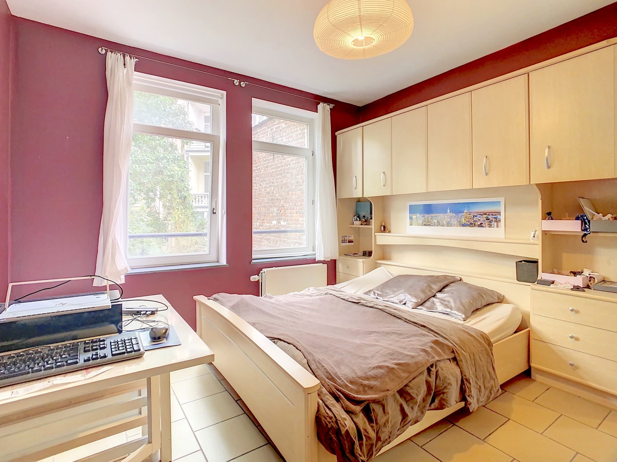 Chambre moderne et cosy avec mur bordeaux, luminosité naturelle et mobilier en bois clair.