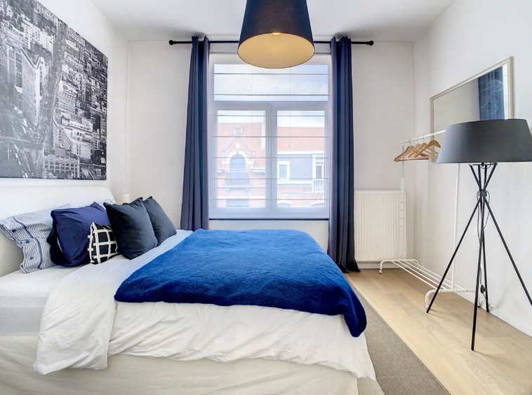Chambre moderne, lumineuse et minimaliste avec lit bleu, œuvre dart urbaine et décoration élégante.