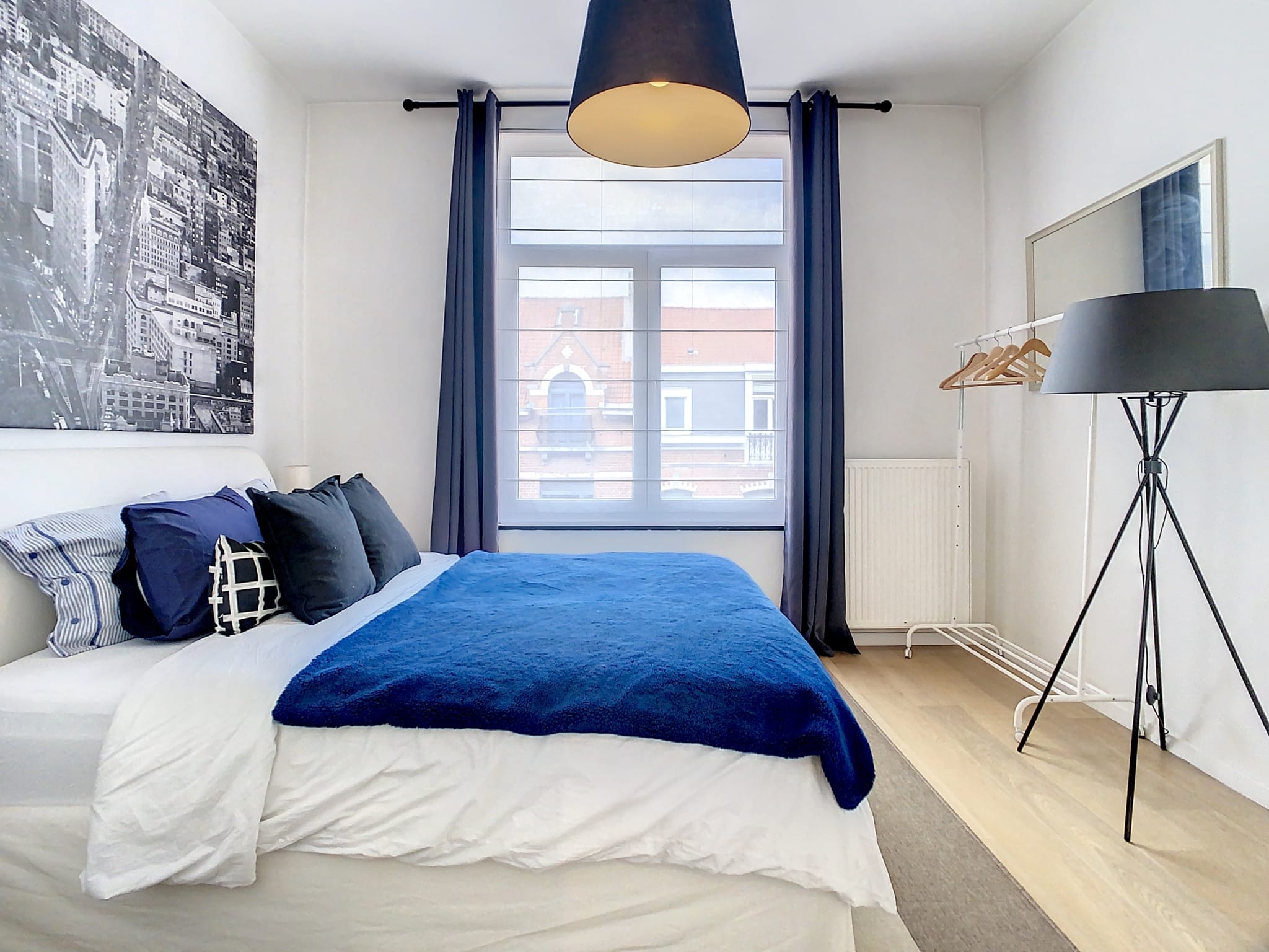 Chambre moderne, lumineuse et minimaliste avec lit bleu, œuvre dart urbaine et décoration élégante.