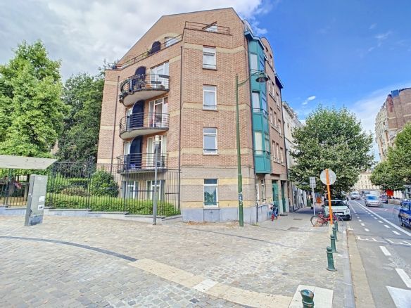Modern residential building with balconies and green gardens, located on a street corner in an urban environment.