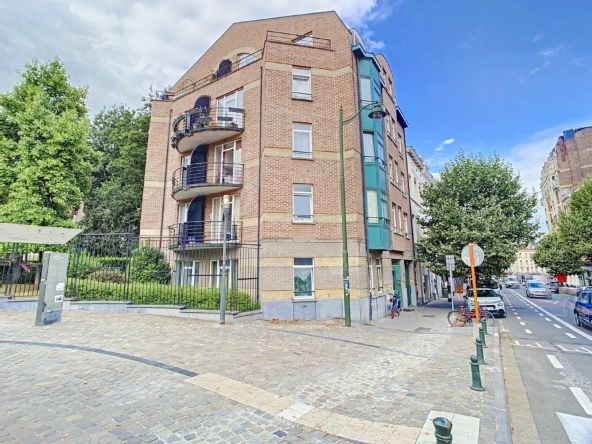 Immeuble résidentiel moderne avec balcons, jardins verts, situé à un coin de rue en environnement urbain.