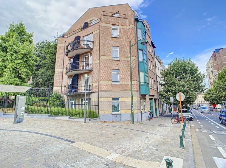 Immeuble résidentiel moderne avec balcons, jardins verts, situé à un coin de rue en environnement urbain.