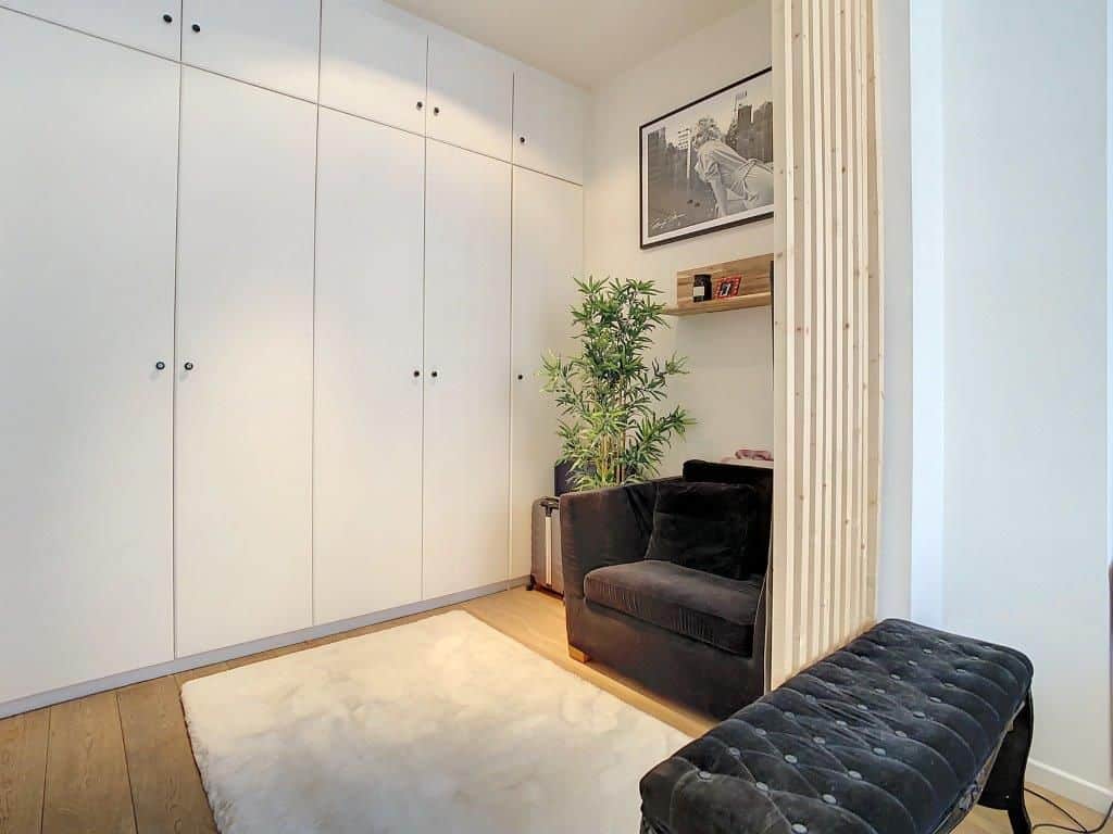 Coin lecture cosy avec meubles modernes, fauteuil noir, armoires blanches et touche de verdure.