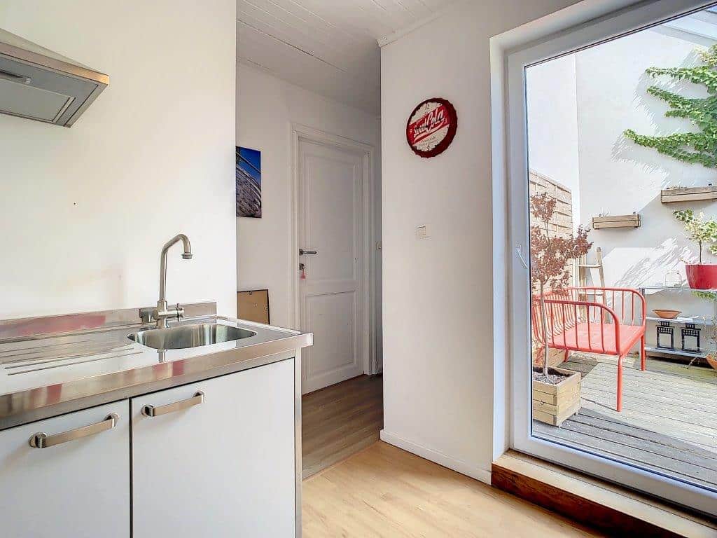 Cuisine moderne lumineuse avec accès extérieur, mobilier blanc, décoration colorée et ambiance chaleureuse.