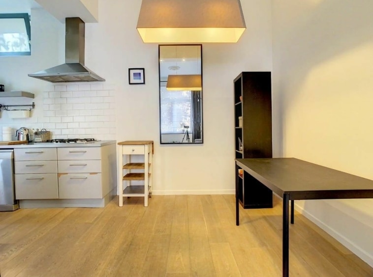 Cuisine minimaliste moderne avec espace de travail, miroir, table noire, parquet en bois chaleureux.