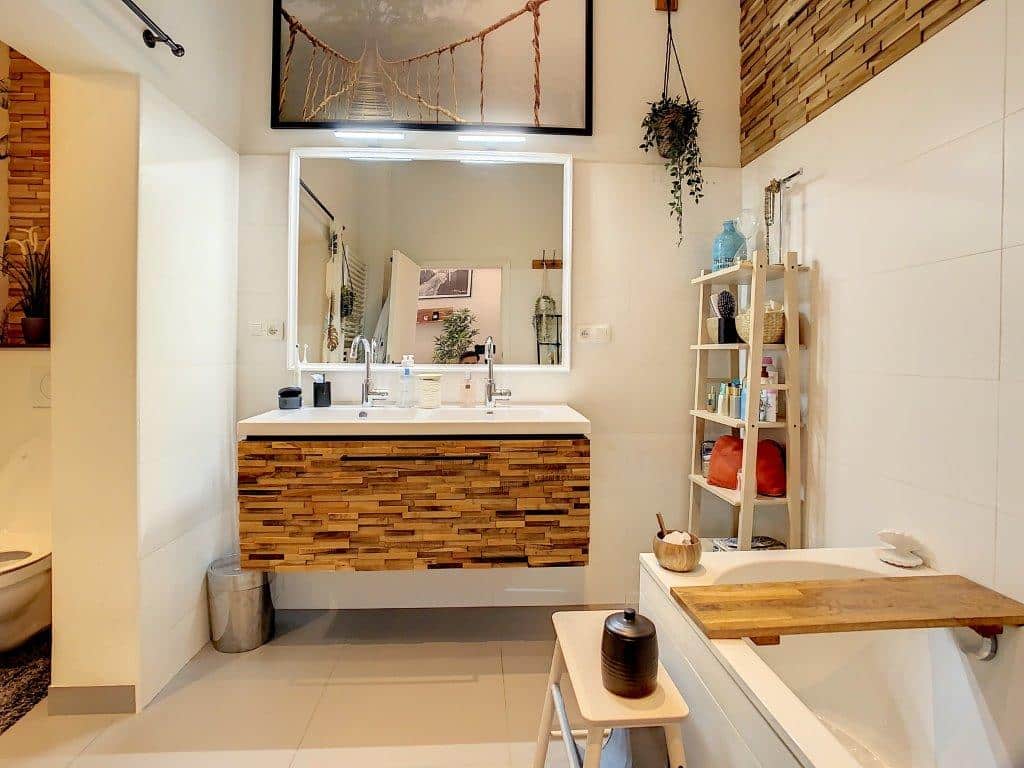 Salle de bain moderne lumineuse avec bois naturel, baignoire, plantes vertes et rangements colorés.