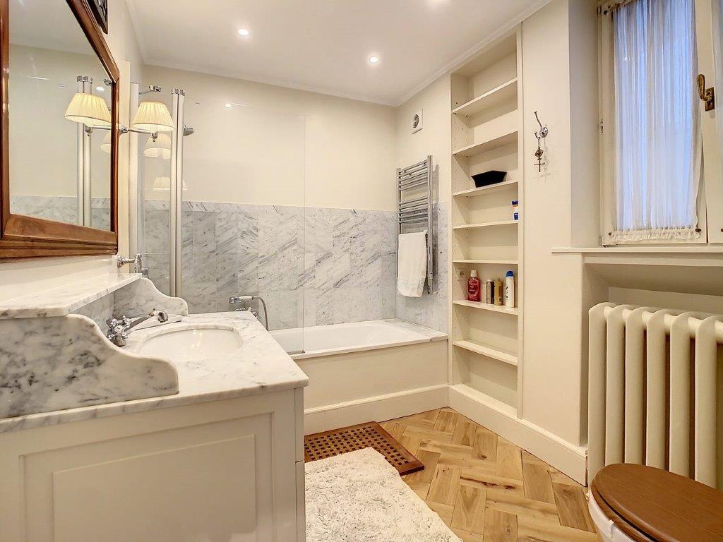 Salle de bain élégante avec marbre, bois chaleureux, baignoire moderne et rangement intégré.
