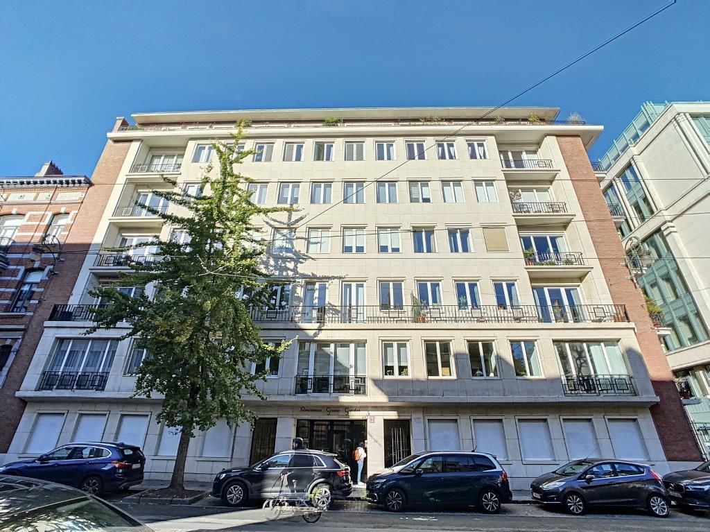 Immeuble résidentiel moderne avec balcons, grande fenestration, arbre vert et ambiance urbaine ensoleillée.