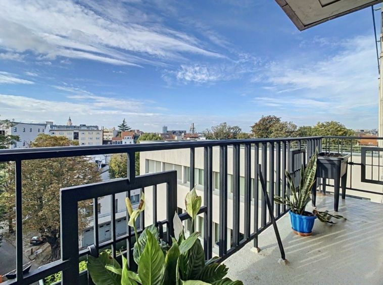 Balcon moderne avec vue sur ville automnale, plantes vertes, ciel bleu et architecture variée.