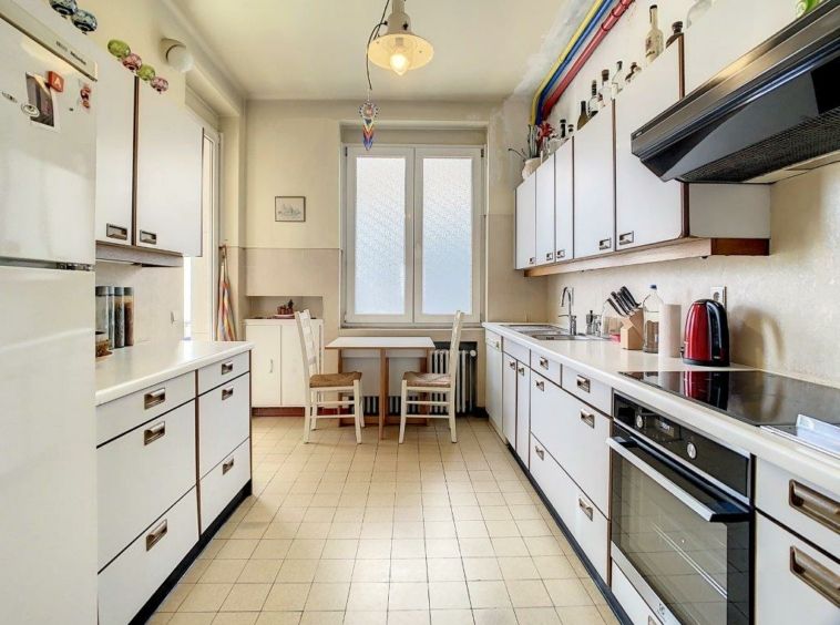 Cuisine lumineuse moderne avec mobilier blanc, espace repas près de la fenêtre, appareils électroménagers.