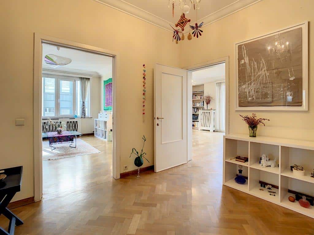 Entrée chaleureuse avec parquet en chevrons, murs jaunes, décor élégant et lumière naturelle abondante.