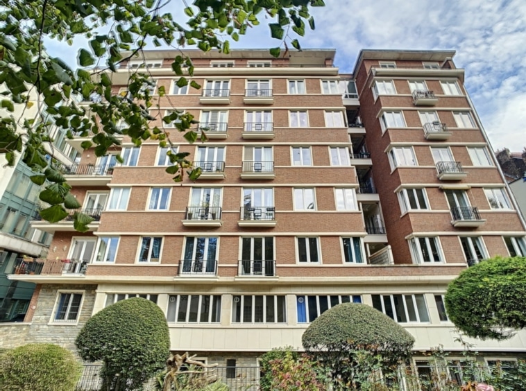 Immeuble résidentiel en brique rouge avec jardins, balcons en fer forgé et ambiance paisible.
