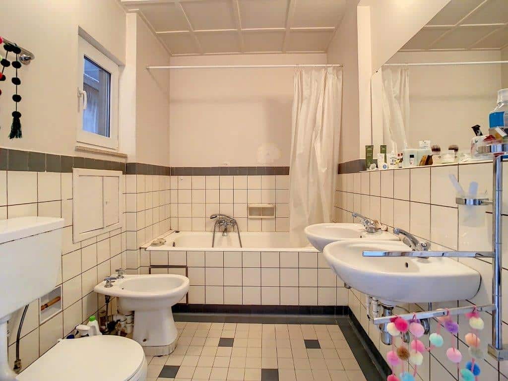 Salle de bain moderne avec douche, deux lavabos, miroir et décoration colorée.