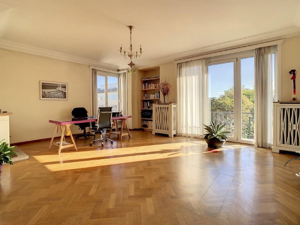 Salle lumineuse avec parquet chevron, bibliothèque, espace de travail, vue extérieure, ambiance chaleureuse.