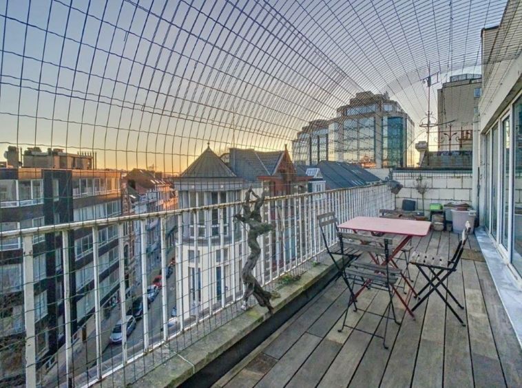 Balcon urbain cosy avec vue sur la ville au coucher de soleil, idéale pour se détendre.