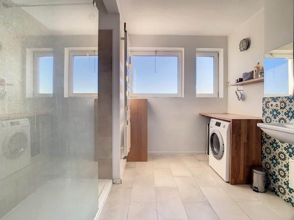 Salle de bain moderne, lumineuse, avec douche, plan en bois et décoration artistique en carrelage.