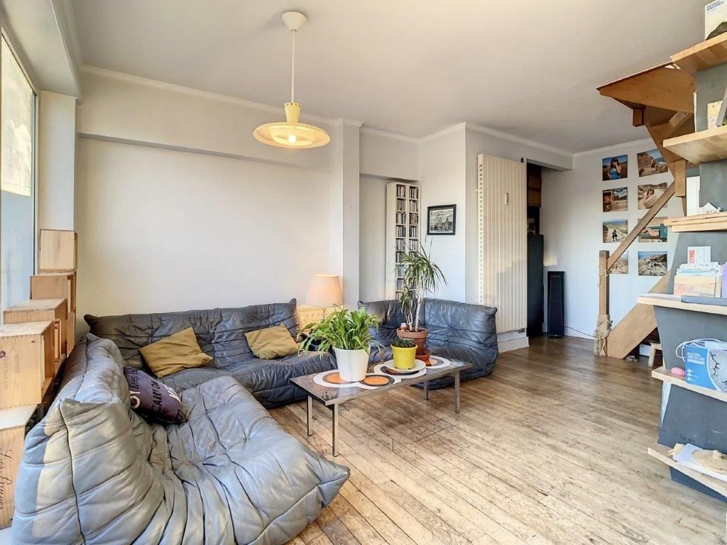 Salon lumineux avec canapé gris, déco chaleureuse, escalier en bois et plantes d’intérieur.