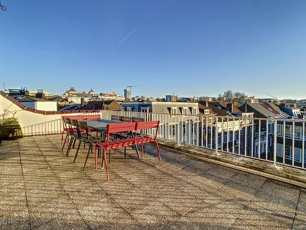 Terrasse ensoleillée avec mobilier rouge, vue urbaine, plantes en pot et ambiance relaxante.