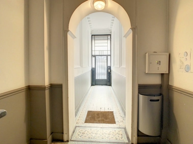 Couloir vintage avec arche, murs blancs et taupe, sol en carreaux, lumière naturelle chaleureuse.