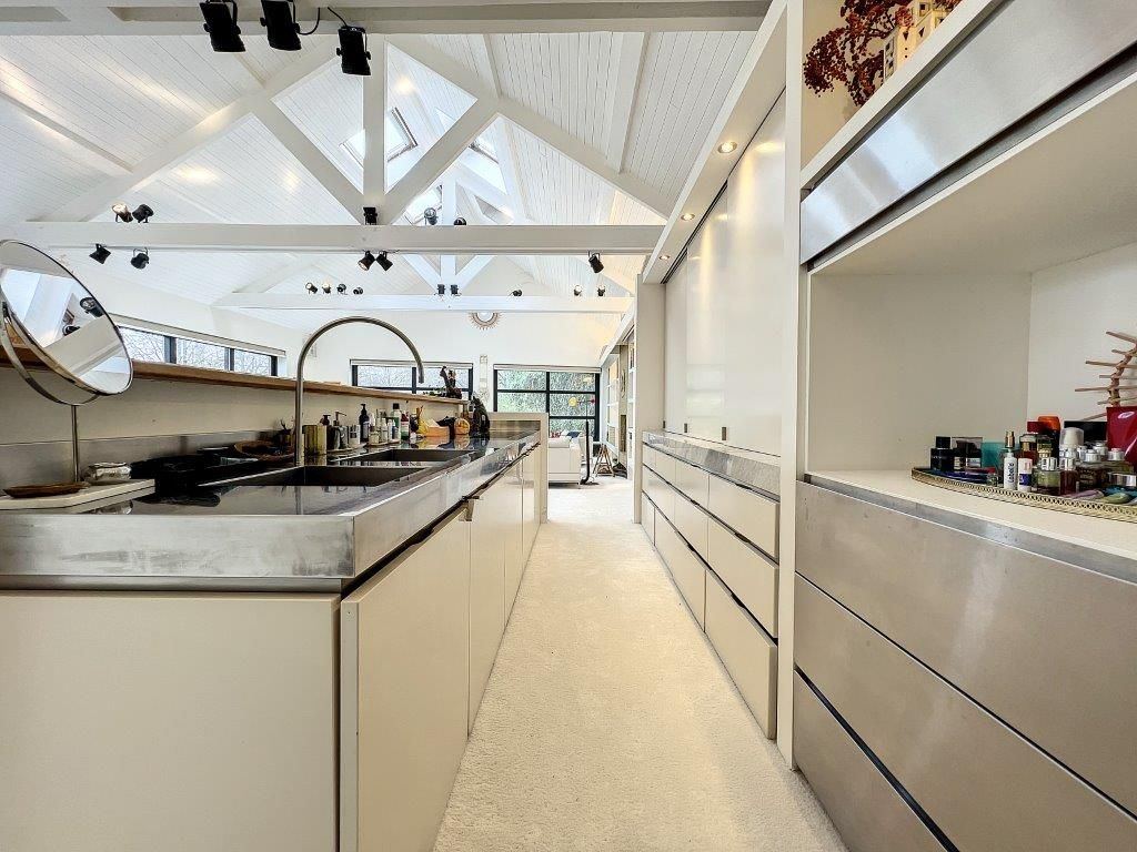 Cuisine moderne lumineuse avec plan en acier, rangements minimalistes et poutres blanches élégantes.