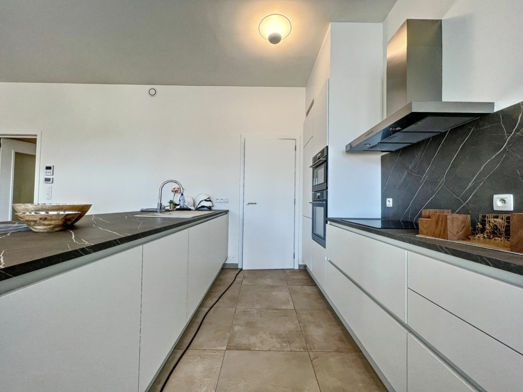 Cuisine moderne minimaliste lumineuse avec plan de travail en bois foncé et mobilier blanc épuré.