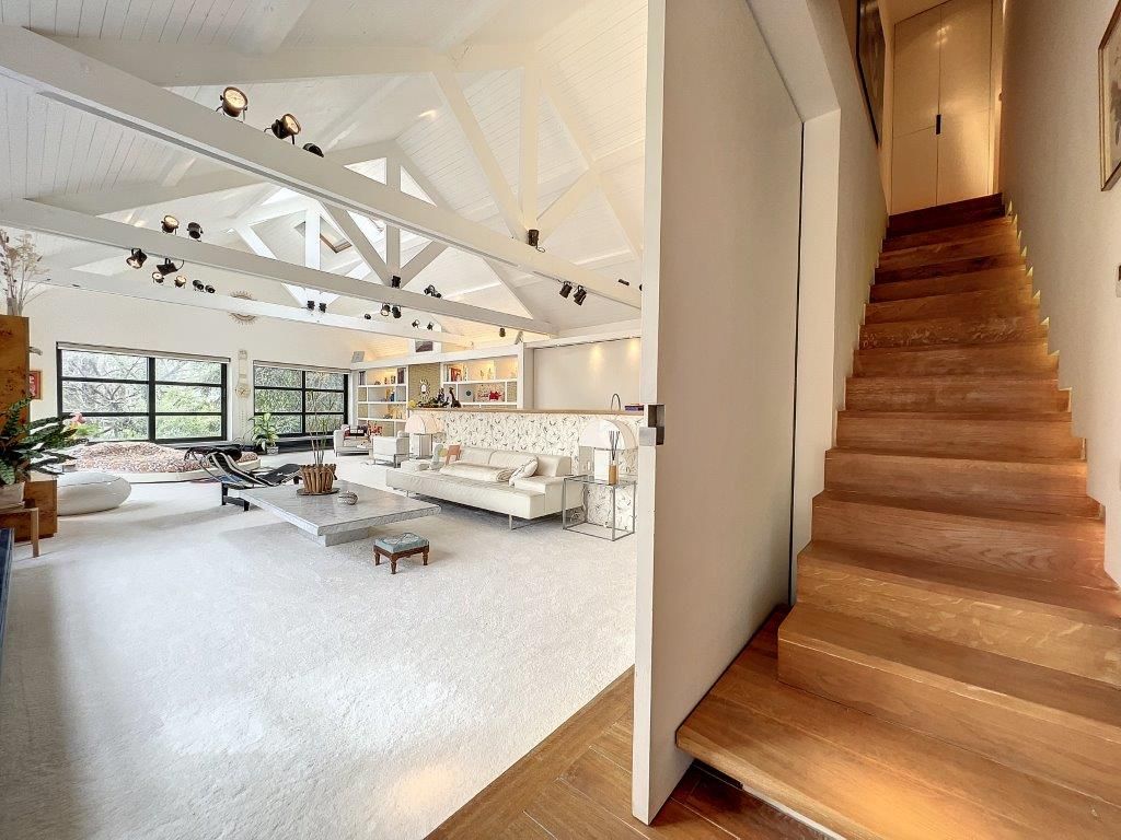 Intérieur contemporain lumineux avec escalier en bois, grandes fenêtres, mobilier minimaliste et ambiance élégante.