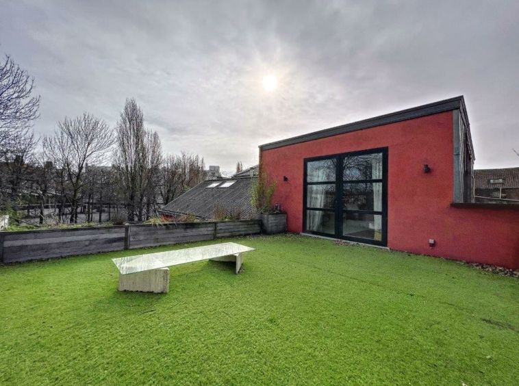 Rooftop garden moderne avec pelouse verte, banc blanc, bâtiment rouge et paysage urbain serein.