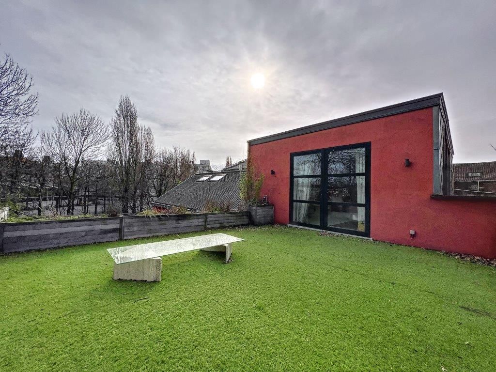 Rooftop garden moderne avec pelouse verte, banc blanc, bâtiment rouge et paysage urbain serein.