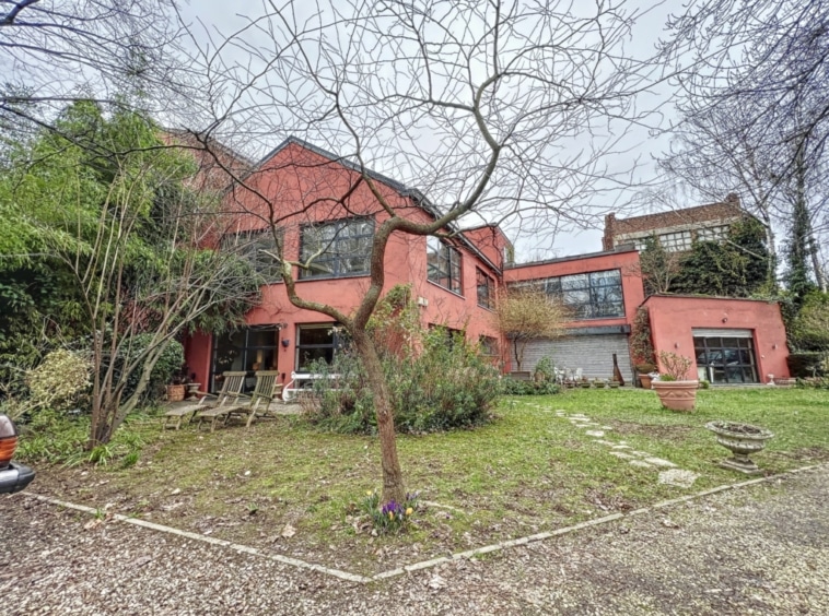 Maison contemporaine colorée avec grandes fenêtres, jardin verdoyant et ambiance paisible.