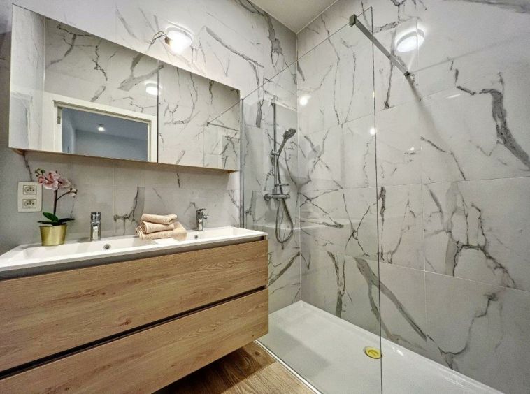 Salle de bain moderne en marbre blanc veiné gris avec meuble en bois et orchidée.