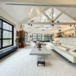 Salon moderne lumineux avec canapés blancs, poutres en bois, plantes vertes et décoration élégante.